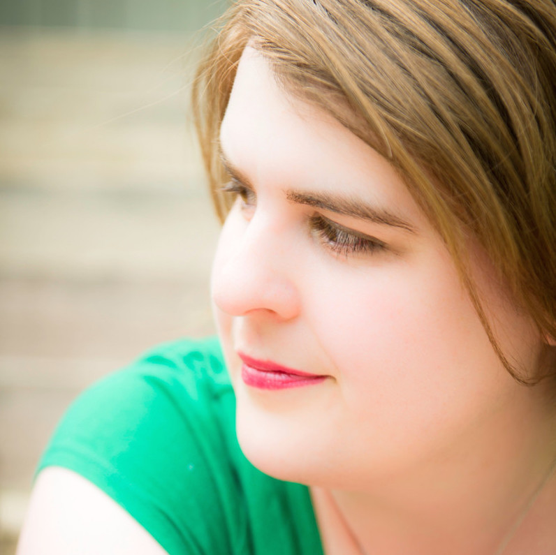 Headshot of white woman with dark blonde hair wearing an emerald green shirt looking off-camera to her right